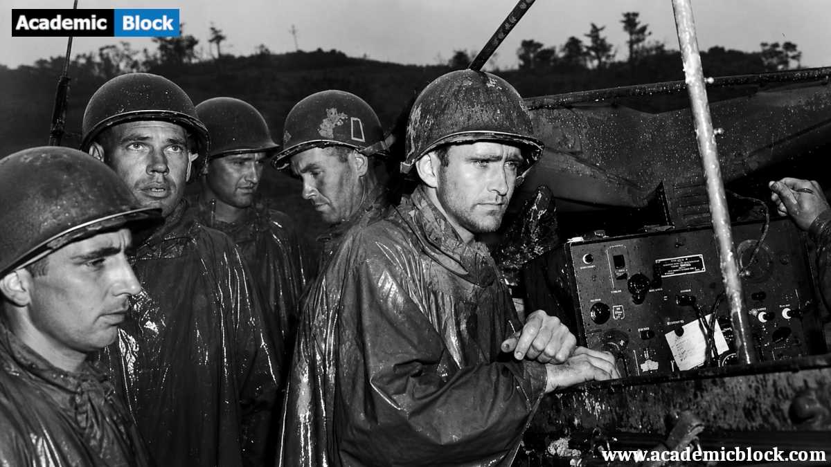 The image shows battle-hardened soldiers of the U.S. Army's 77th Infantry Division on Okinawa listening to radio reports of Germany's surrender on May 8, 1945, before resuming combat.