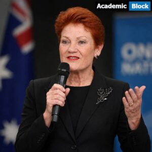 Pauline Hanson speaking at a public event, holding a microphone and wearing a black suit with a brooch, against a blurred political backdrop.