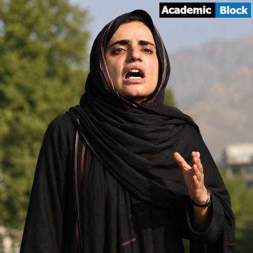 Mahrang Baloch speaks passionately during a public gathering, wearing a black dress and headscarf against an outdoor background.