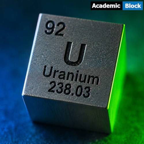 Close-up of a metallic cube engraved with Uranium's symbol, atomic number 92, and atomic weight 238.03, illuminated with green and blue lighting.