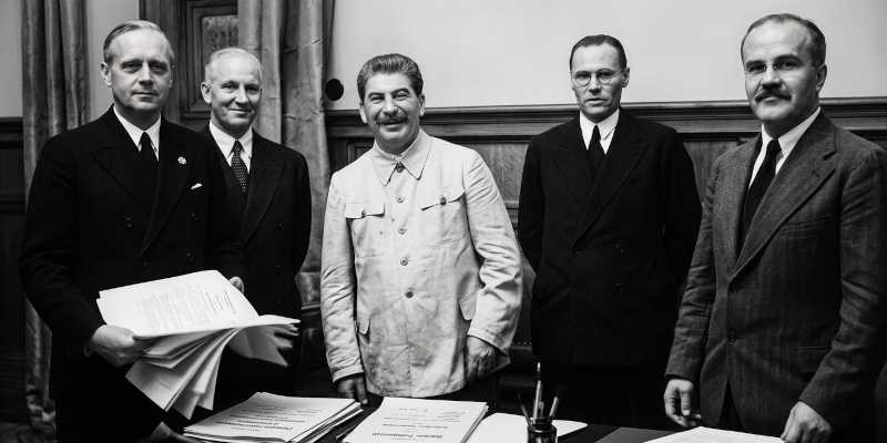 Historical image showing Joseph Stalin and officials at the signing of the Molotov-Ribbentrop Pact.